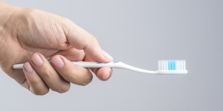 Close-Up Of Hand Holding Toothbrush Over White Background