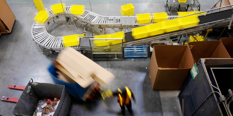 Image: An employee pulls a pallet jack past plastic crates moving along a conveyor at the Amazon.com Inc. fulfillment center in Robbinsville, N.J., on June 7, 2018.
