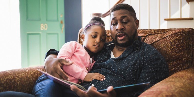 Father and daughter reading book in living room at home