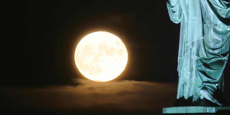 The full Sturgeon Blue Moon rises next to the Statue of Liberty in New York on Aug. 22, 2021.