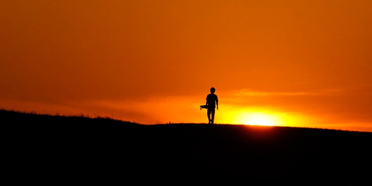 A skateboarder walks through a park at sunset on June 8, 2022, in San Antonio, as temperatures in South Texas continued to top the 100 degree mark.