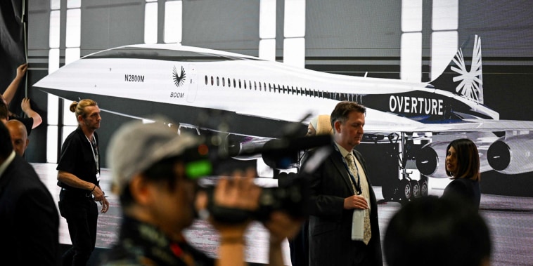 Attendees walk past a poster of a Boom Supersonic concept Overture aircraft at the Farnborough Airshow, in Farnborough, England, on July 18, 2022.