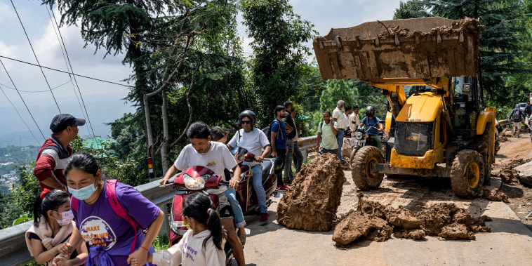 People rush past an earthmover clearing a road of a big rock that came down with mud and plant debris following intense monsoon rains in Dharamshala, Himachal Pradesh state, India, on Aug. 21, 2022.