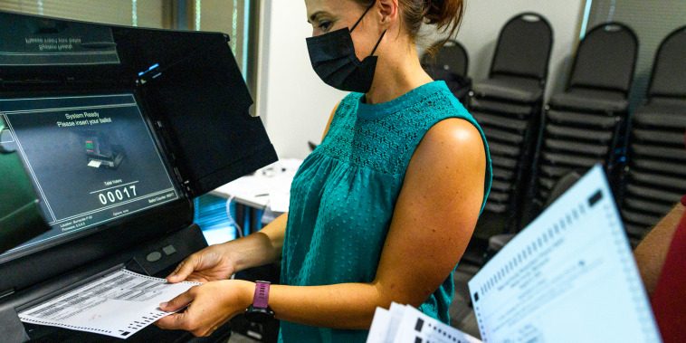Election judges submit test ballots into a machine