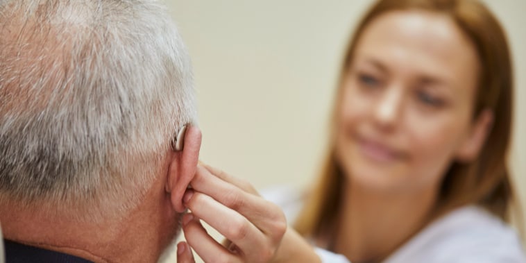 Doctora aplicando un audífono en el oído de un hombre mayor.