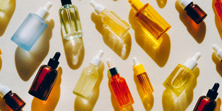 Set of many different glass bottles with cosmetic liquids on white surface. Play of light creates abstract patterns from shadows and illuminating yellow reflections. Trendy colors of the year 2021. Flat lay style