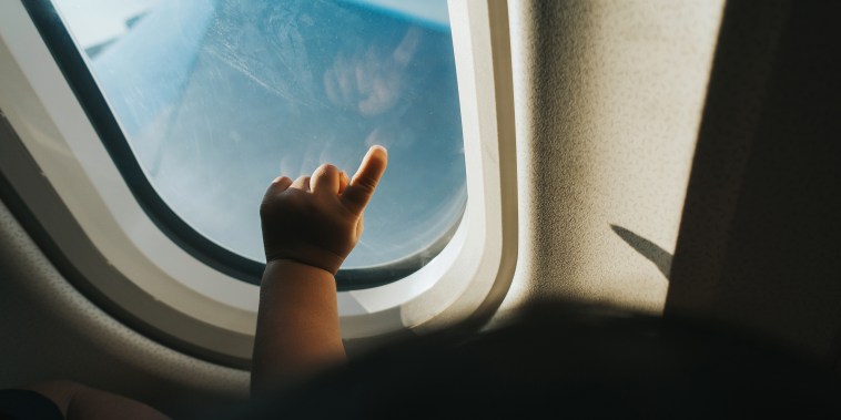 Cropped hand of a toddler pointing airplane window against blue sky while travelling