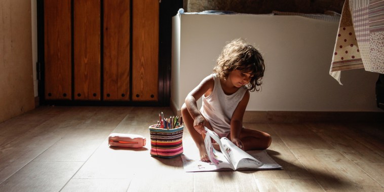 Little girl sitting on the floor at home while drawing and coloring on a paper.