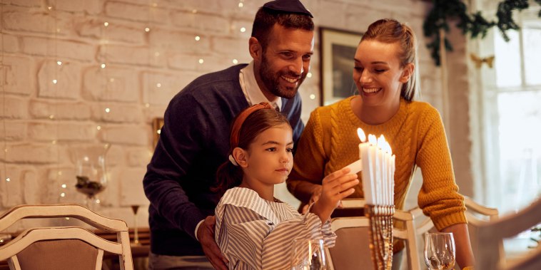 Happy Jewish family lightning the menorah before a meal at dining table.