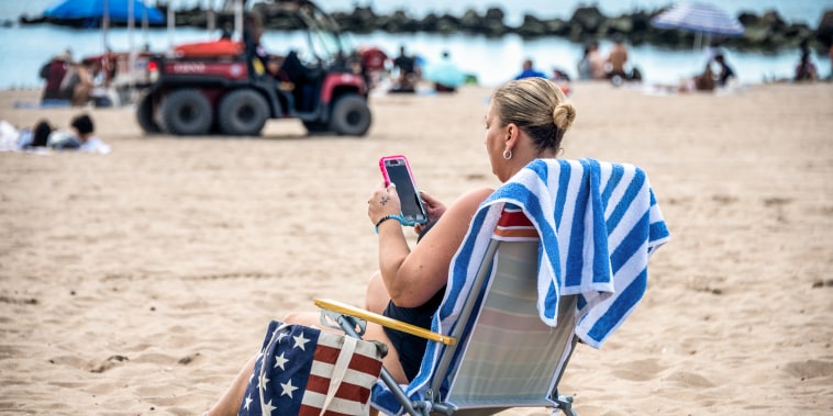 Image: A woman looks at her phone while sitting on the beach at Coney Island on Sept. 4, 2021 in New York City.