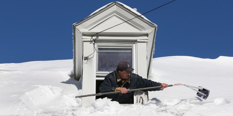 A resident uses a rake to clear snow from the roof from his attic window in East Boston.