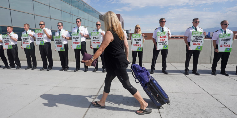 A traveler walks pass Delta Air Lines pilots picketing at Salt Lake City International Airport on June 30, 2022. 