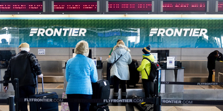 Travelers wait in line at the Frontier Airlines check-in counter at Denver International Airport