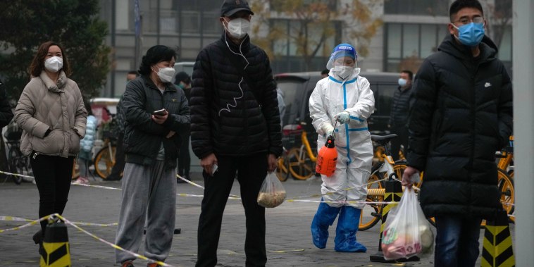 Un trabajador con traje protector rocía desinfectante mientras los residentes hacen fila para sus muestras de garganta de COVID-19 de rutina en un sitio de prueba de coronavirus en Beijing, el jueves 24 de noviembre de 2022.