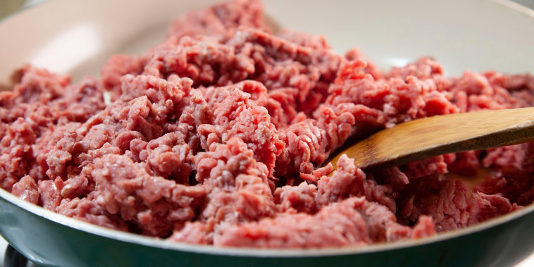 Close up of a wooden spoon in raw ground beef in a frying pan