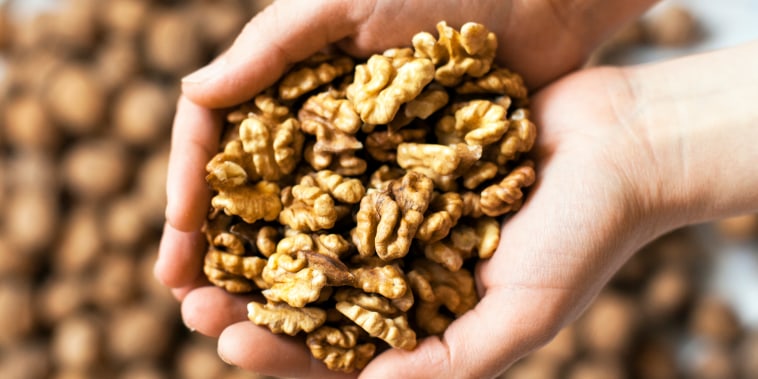 Handful of walnuts kernels against the walnuts in shell background.