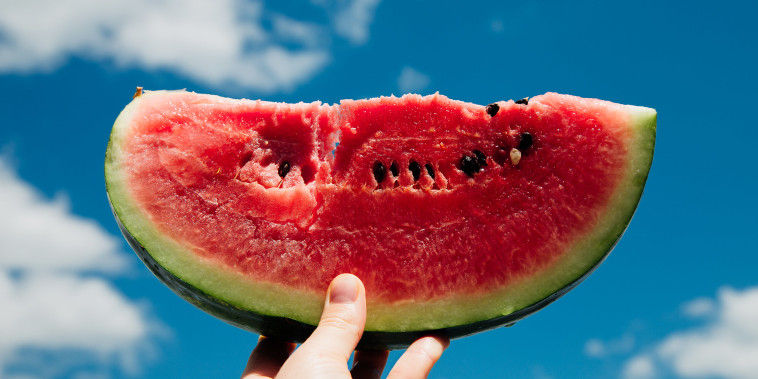 Slice of watermelon in hand over sky background