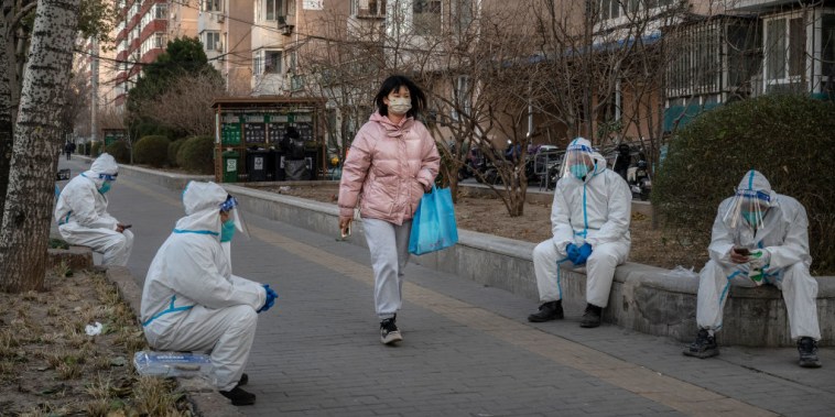 Un peatón camina junto a trabajadores de control de epidemias que trabajan en saneamiento y llevan EPI para protegerse de la propagación del COVID-19, el 6 de diciembre de 2022 en Pekín, China. 