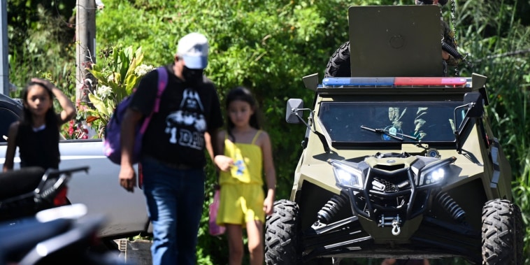 Una mujer con dos niñas pequeñas camina frente a un vehículo militar blindado que patrulla Soyapango, la segunda ciudad más poblada de El Salvador, después de que se ordenara una movilización de fuerzas de seguridad para cercar la zona en un afán de combatir las pandillas. Es el 4 de diciembre de 2022