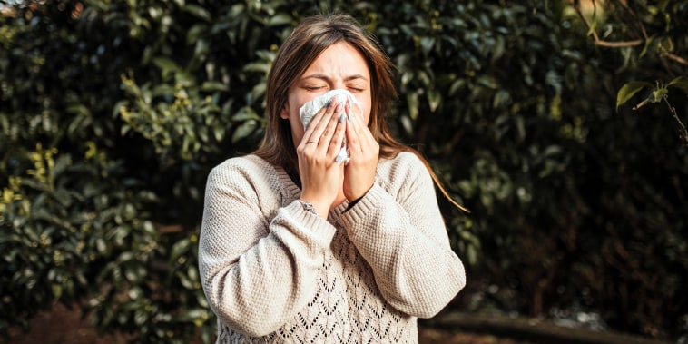 young woman suffering from flu symptoms and blowing her nose.