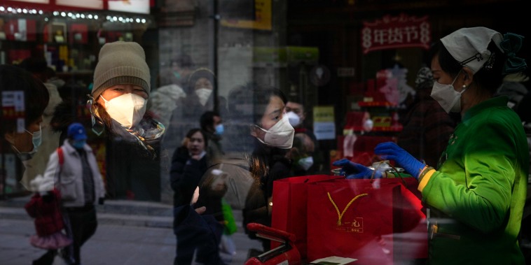 Gente reflejada en una ventana mientras visitantes con mascarilla compran productos de té en Qianmen, un lugar turístico popular en Beijing, martes, 3 de enero de 2023. 
