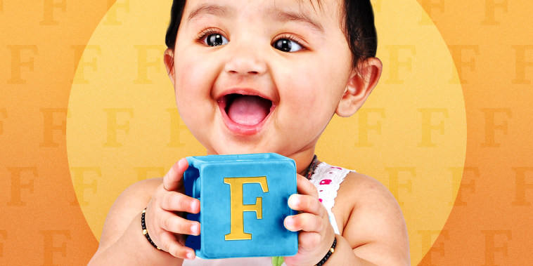 baby girl holding on to an alphabet block with the letter F on it