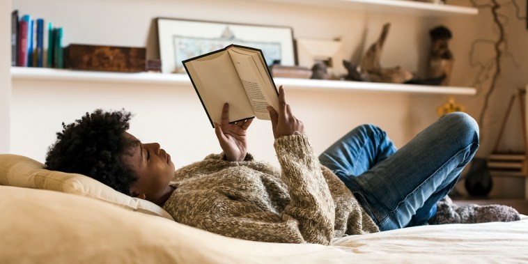 Young woman lying on bed reading a book.