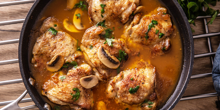 Top view of chicken thighs with bones cooked with mushrooms in a rich sauce, served in a pan.