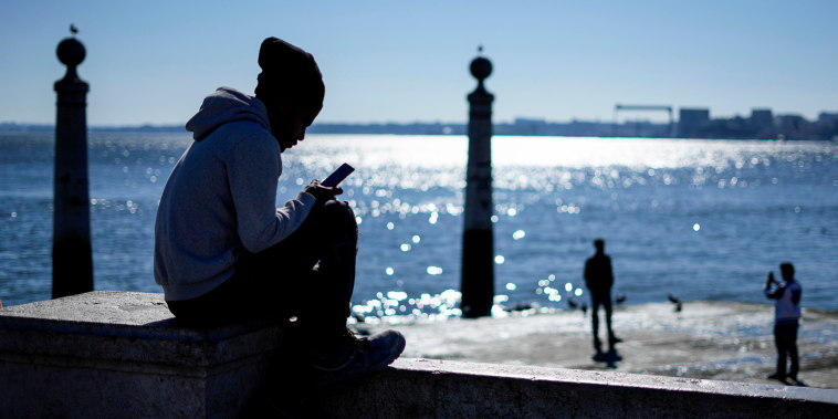 A young man checks his phone by the Tagus river at Lisbon's Comercio square on Jan. 30, 2023.