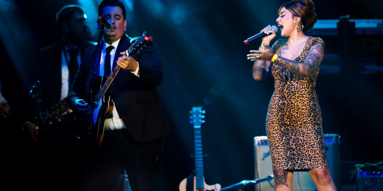 Una mujer con micrófono canta música soul al lado de un hombre trajeado en la guitarra durante un concierto en Los Ángeles en diciembre de 2021
