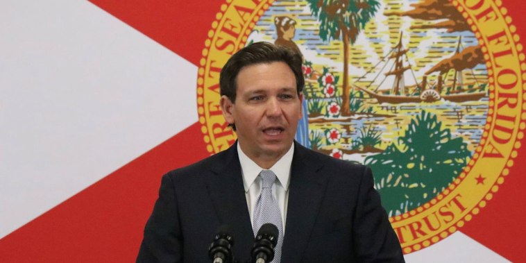 Ron DeSantis habla desde un podio con micrófonos y frente a una pantalla que muestra la bandera estatal de Florida