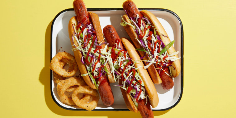 Three hotdogs on tray with onion rings, overhead view on yellow background