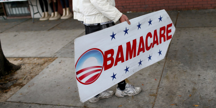 Image: Pedro Rojas holds a sign directing people to an insurance company where they can sign up for the Affordable Care Act, also known as Obamacare