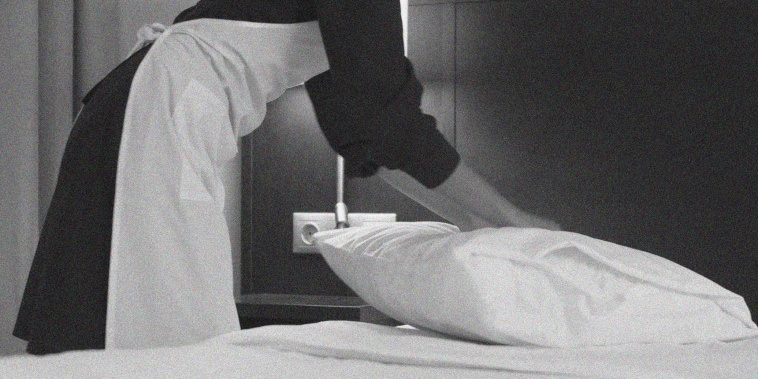 A member of the house cleaning staff makes a bed in a hotel room.