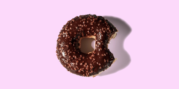 Close up view of bitten chocolate donut on pink background isolated. Food and health concept.
