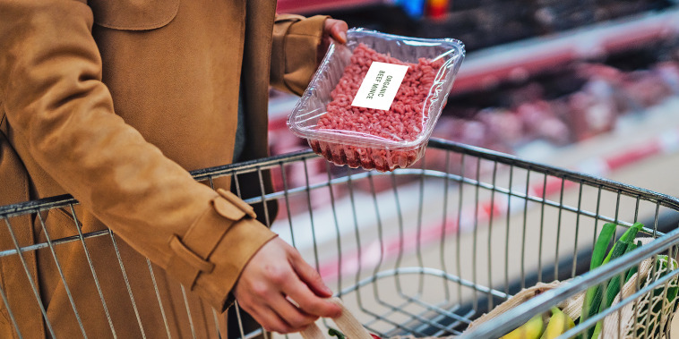 Young woman placing a pack of fresh minced beef in shopping cart.