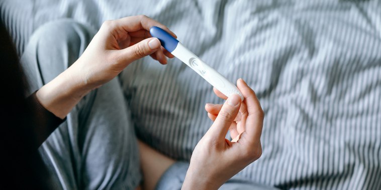 View of disappointed young woman sitting on the bed and holding a negative pregnancy test.