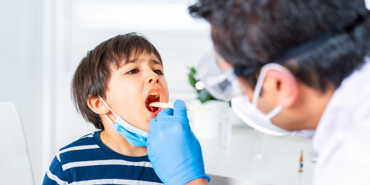 Pediatrician examining child patient’s throat at clinic.