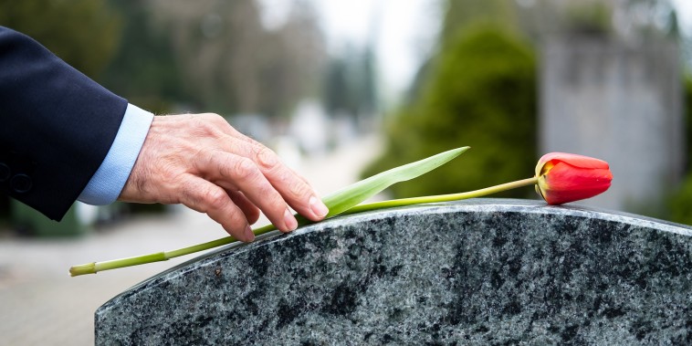Man putting flower on tombstone at cemetery.