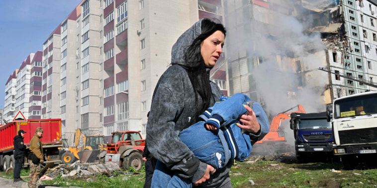 A woman walks past damaged residential buildings as she carries a child in Uman, Ukraine.