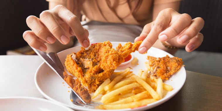 Woman picking at fried chicken and fries.