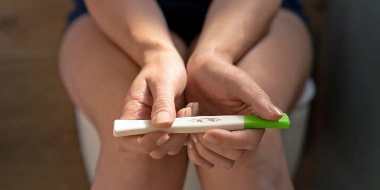 Close up of woman sitting holding pregnancy test stick.