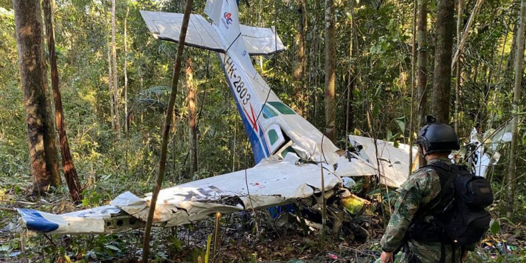 In this photo released by Colombia's Armed Forces Press Office, a soldier stands in front of the wreckage of a Cessna C206, Thursday, May 18, 2023, that crashed in the jungle of Solano in the Caqueta state of Colombia.  A search continues for four Indigenous children who may have survived the deadly plane crash in the Amazon jungle on May 1. On Tuesday, May 16, soldiers found the wreckage and the bodies of three adults, including the pilot and the children's mother.