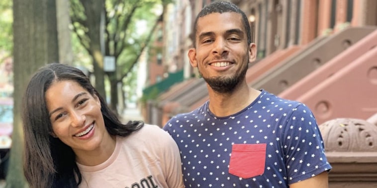 A young woman in a pink "make good trouble" shirt laughs on the street in New York. A young man in a blue shirt with white stars and red pocket smiles next to her.