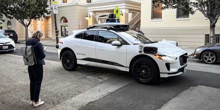 Waymo communications manager Julia Ilina stands next to a Waymo driverless taxi that stopped in the street because the back door was not completely shut, while traffic backed up behind it, in San Francisco, on Feb. 15, 2023. 