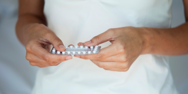 Woman holding birth control pills, mid section