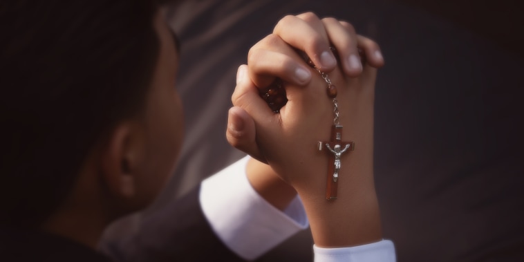 A young boy holding Catholic rosary beads.