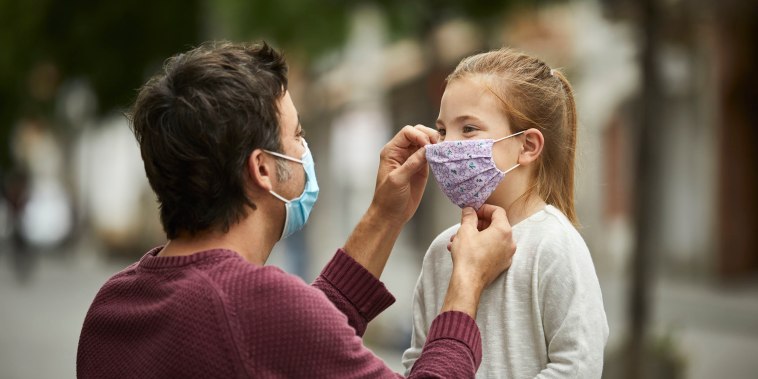 Father with surgical face mask, is putting a hand made protective face mask on his little daughter for the COVID-19 pandemic.