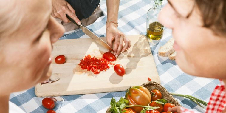 Person cutting tomatoes on table with friends in foreground. 