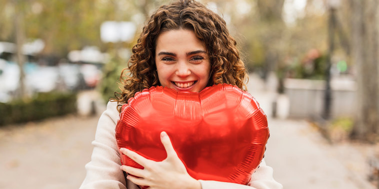 Happy young woman hugging red heart shaped balloon